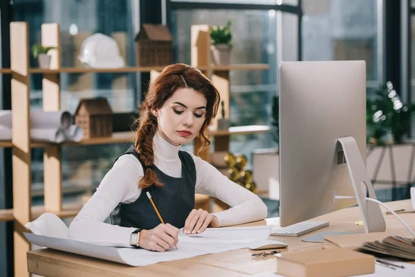 Female architect drawing building plan at workplace with computer — Stock Photo