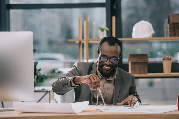 Afrikanischer amerikanischer Architekt zeichnet Baupläne mit Kompass im Büro — Stockfoto