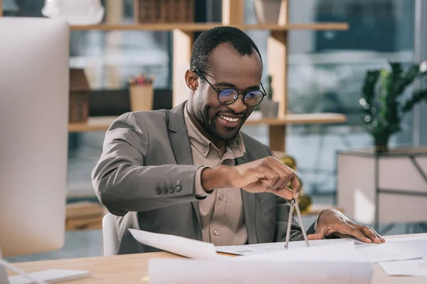 African american architect drawing blueprints with compasses in modern office — Stock Photo