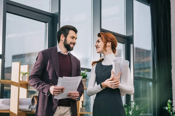 Dos arquitectos felices trabajando con planos y documentos en la oficina - foto de stock