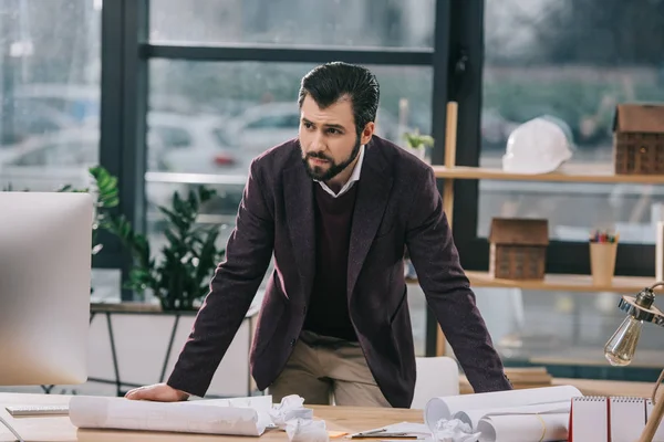 Thoughtful male architect at workspace with blueprints and crumpled papers — Stock Photo