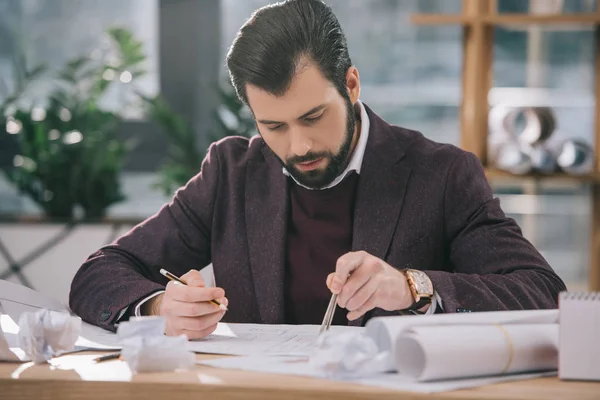 Architect drawing building plans with compasses at workplace with crumpled papers — Stock Photo