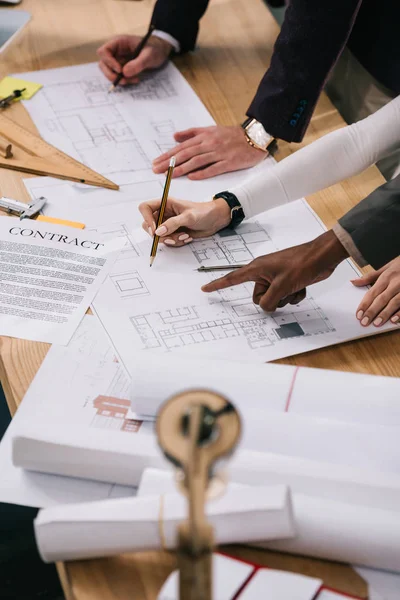 Cropped view of multiethnic architects discussing documents and drawing blueprints in office — Stock Photo