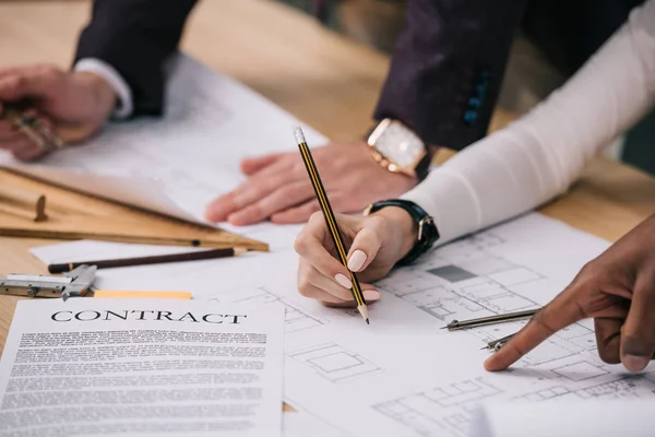 Cropped view of multiethnic architects discussing and working with blueprints and documents in office — Stock Photo