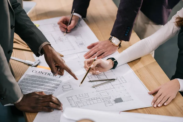 Cropped view of multiethnic architects discussing and working with blueprints and documents in office — Stock Photo