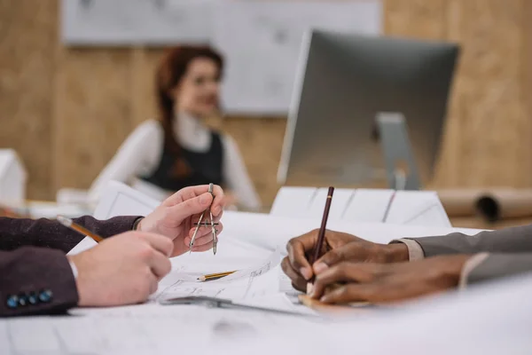 Arquitectos dibujando planos juntos mientras su colega trabaja con la computadora - foto de stock