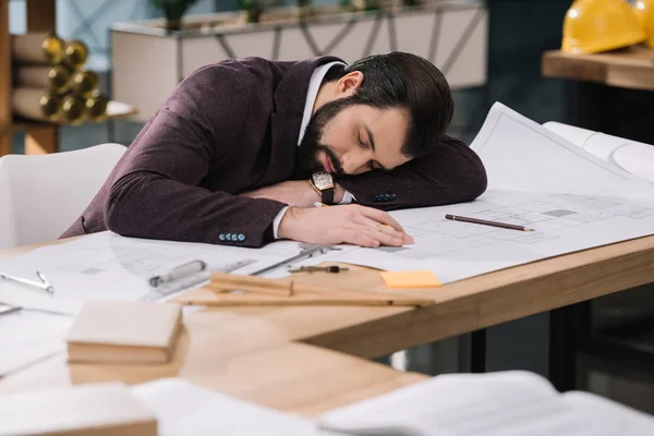 Giovane architetto oberato di lavoro dormire su piani di costruzione sul posto di lavoro — Foto stock