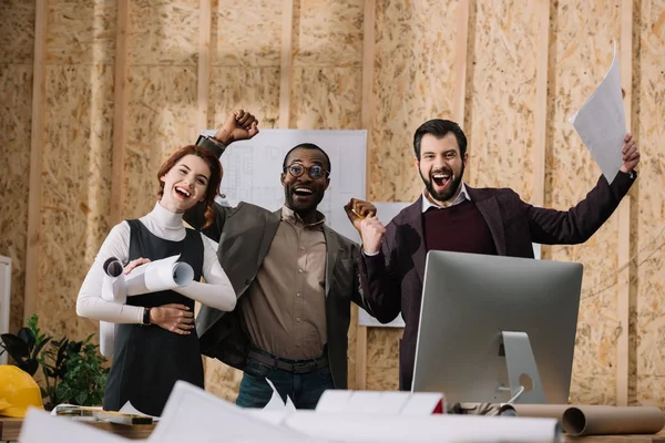 Equipe comemorativa multiétnica de arquitetos com papéis no escritório moderno — Fotografia de Stock