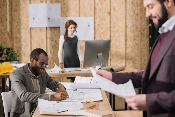 Equipo de arquitectos que trabajan con planos de edificios en oficinas modernas - foto de stock