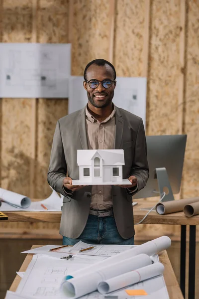 Joven arquitecto afroamericano con modelo de casa de papel en la oficina - foto de stock