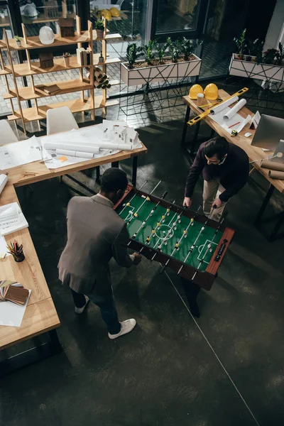 Высокий угол зрения мультиэтнических архитекторов, играющих в настольный футбол в офисе — стоковое фото