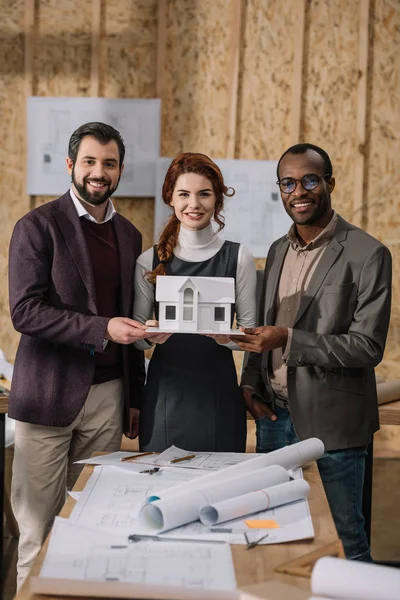 Jeune équipe multiethnique d'architectes tenant un modèle miniature de bâtiment — Photo de stock