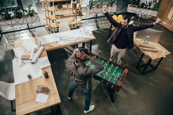 Vista de ángulo alto de los jóvenes arquitectos jugando futbolín en la oficina - foto de stock