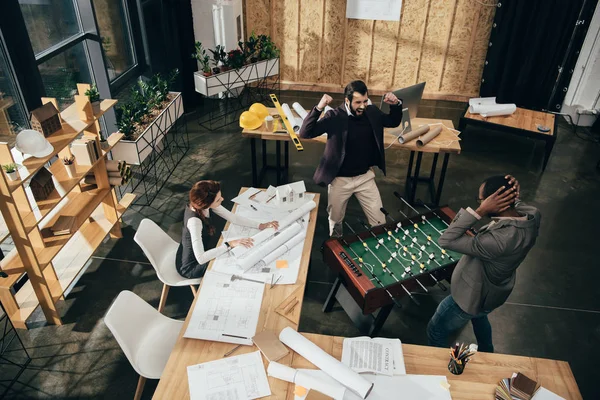 Высокий угол обзора молодых архитекторов, играющих в настольный футбол в современном офисе — стоковое фото