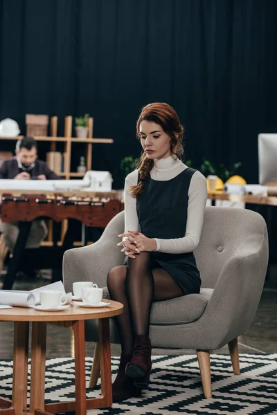 Молода красива бізнес-леді сидить на кріслі і дивиться на папери на столі — стокове фото