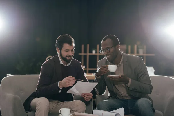 Hombres de negocios sentados en sillones con café y discutiendo documentos - foto de stock