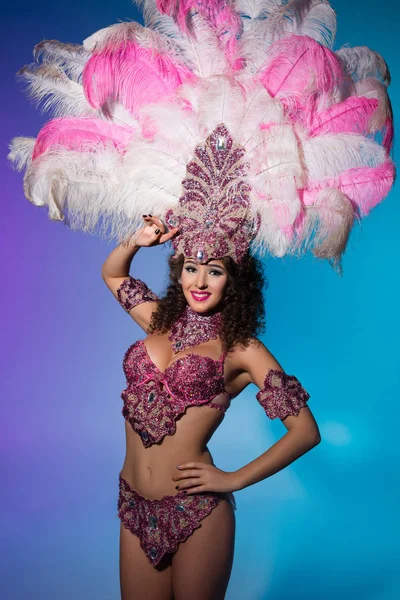 Яркая женщина в карнавальном костюме с розовыми перьями позирует эмоционально на синем фоне — стоковое фото