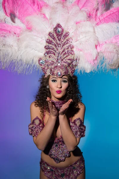Mujer brillante en traje de carnaval con plumas rosas enviando beso de aire aislado sobre fondo azul - foto de stock