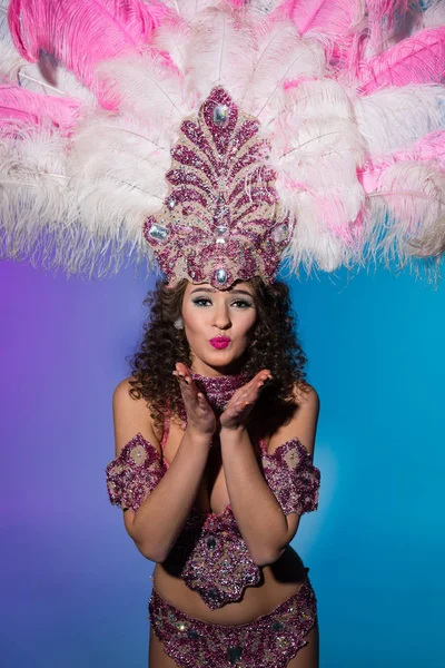 Femme lumineuse en costume de carnaval avec des plumes roses envoyer baiser d'air isolé sur fond bleu — Photo de stock