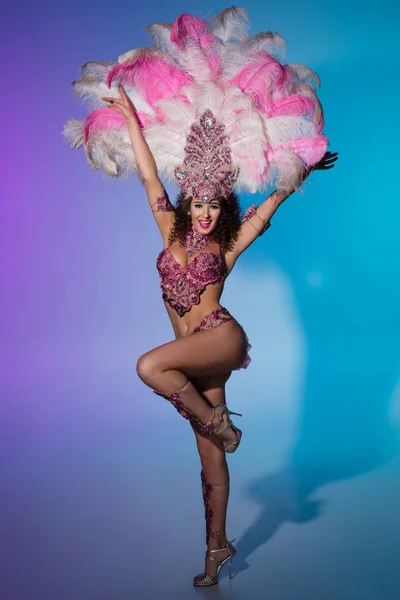 Яркая женщина в карнавальном костюме с розовыми перьями выступает на синем фоне — стоковое фото