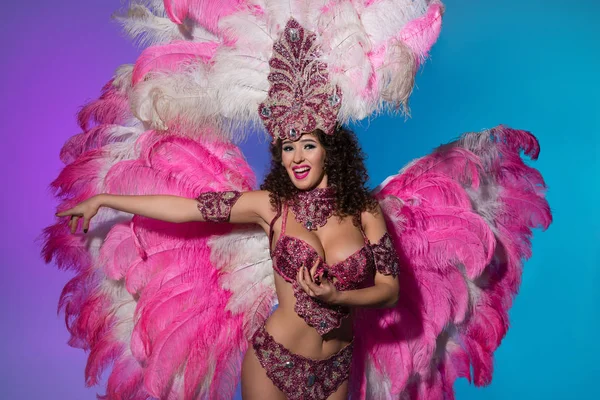 Mujer brillante en traje de carnaval con plumas rosas realizando danza aislada sobre fondo azul - foto de stock