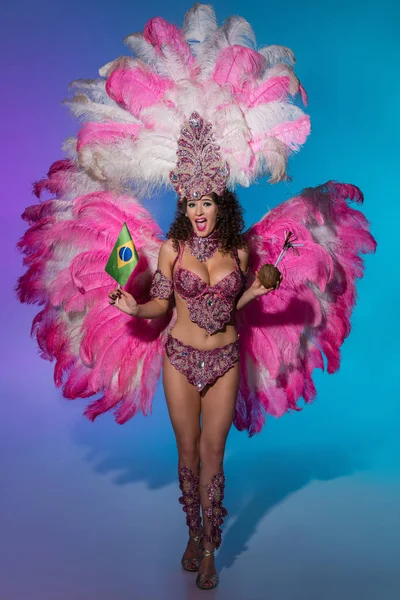 Mulher alegre em traje de carnaval com penas rosa segurando coco e bandeira do Brasil em fundo azul — Fotografia de Stock