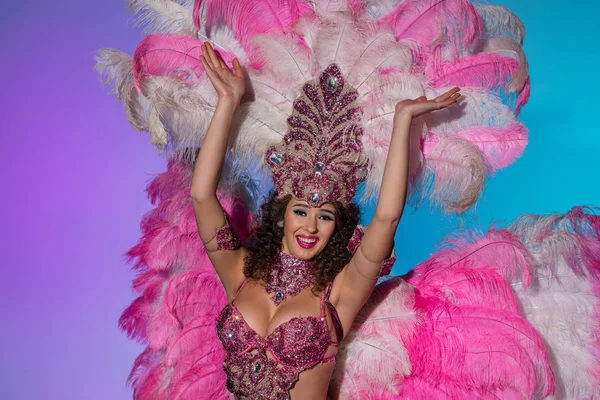 Mujer joven feliz en traje de carnaval con plumas rosadas sonriendo eufórico aislado sobre fondo azul - foto de stock