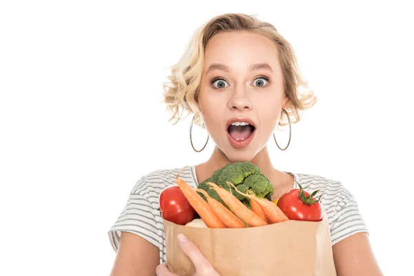 Surprised young woman holding grocery bag and looking at camera isolated on white — Stock Photo
