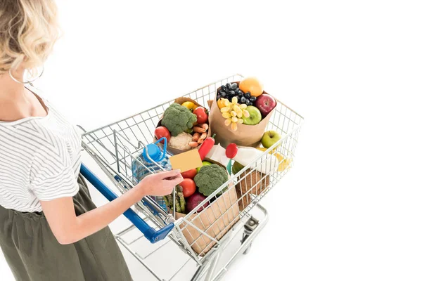 Cropped shot of woman holding credit card and shopping trolley with grocery bags isolated on white — Stock Photo