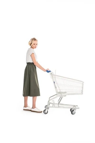 Full length view of upset young woman standing with empty shopping cart isolated on white — Stock Photo