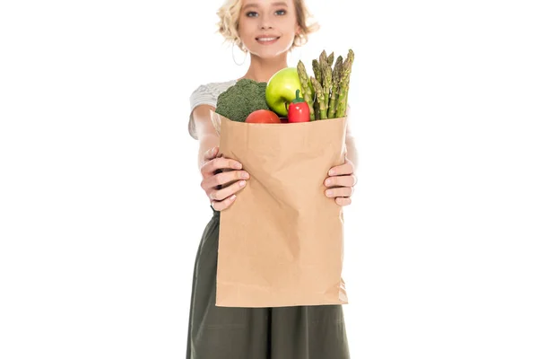 Hermosa joven mujer sosteniendo bolsa de comestibles y sonriendo a la cámara aislada en blanco - foto de stock