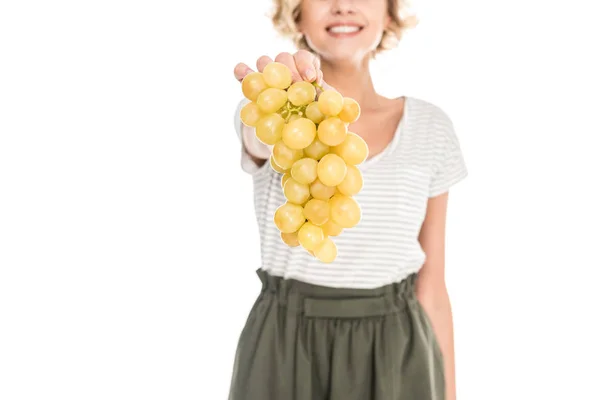 Крупным планом частичный вид улыбающейся молодой женщины, держащей свежий спелый виноград изолированный на белом — стоковое фото