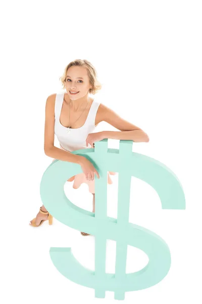 Високий кут зору усміхненої жінки, що спирається на знак долара і дивиться на камеру ізольовано на білому — стокове фото