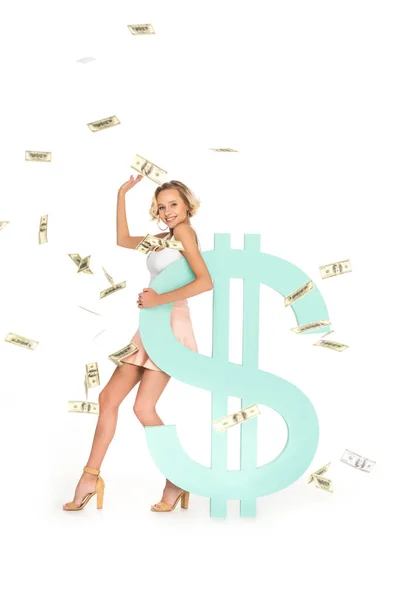 Smiling young woman leaning on dollar sign with falling dollars around isolated on white — Stock Photo