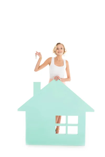 Young woman with keys in hand standing near house model isolated on white — Stock Photo