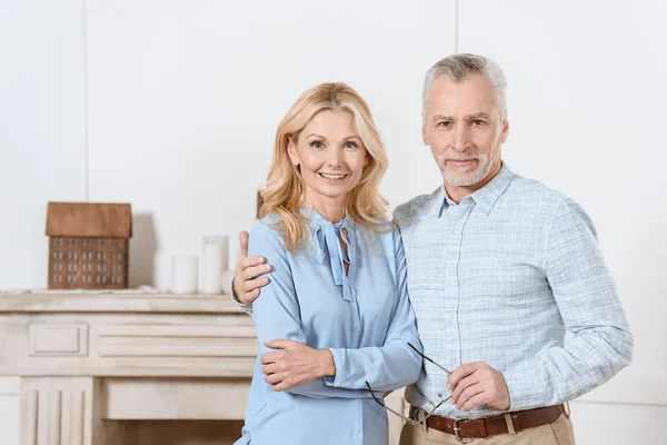 Mature man and woman hugging by fireplace in cozy room — Stock Photo