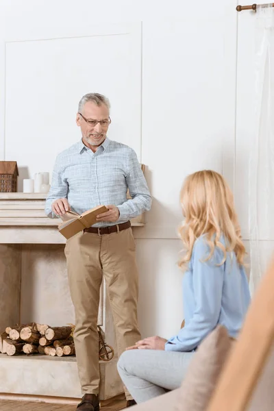 Reifer Mann liest Buch und diskutiert mit Frau im hellen Raum — Stockfoto