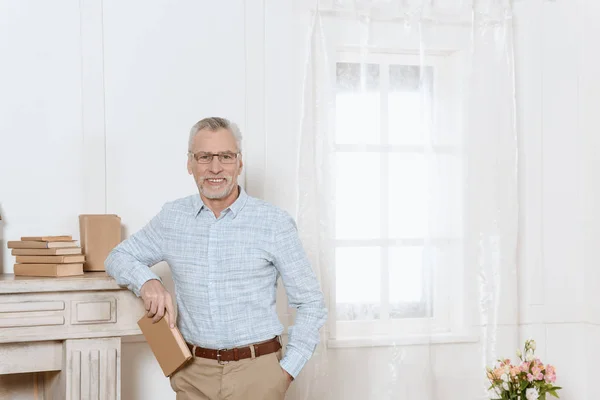 Senior man stands by fireplace in room holding a book — Stock Photo