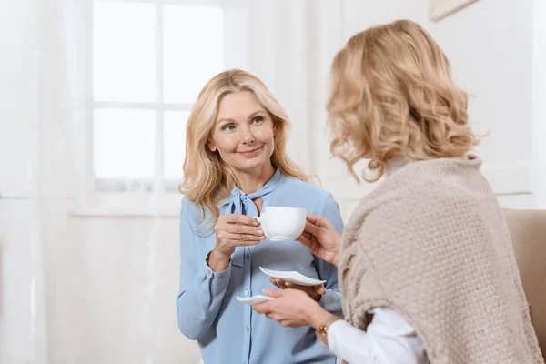 Two middle aged women sitting on sofa and drinking tea — Stock Photo