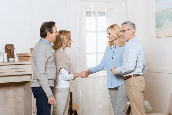 Пара мужчин и женщин среднего возраста приветствуют своих друзей в качестве гостей и пожимают друг другу руки — стоковое фото