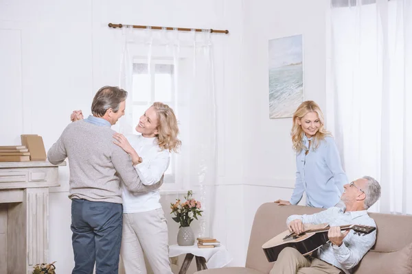 Hombres y mujeres mayores escuchando música de guitarra y bailando en la sala de estar - foto de stock