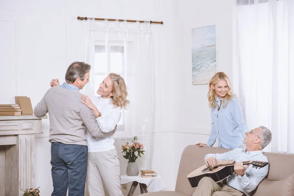 Hommes et femmes âgés écoutant de la musique de guitare et dansant dans le salon — Photo de stock