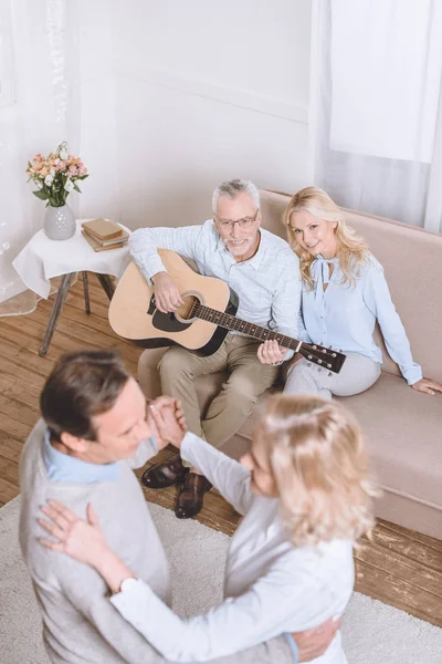 Hombres y mujeres mayores escuchando música de guitarra y bailando en la sala de estar - foto de stock