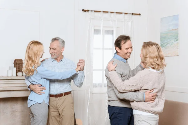Middle aged men and women dancing by fireplace in cozy room — Stock Photo
