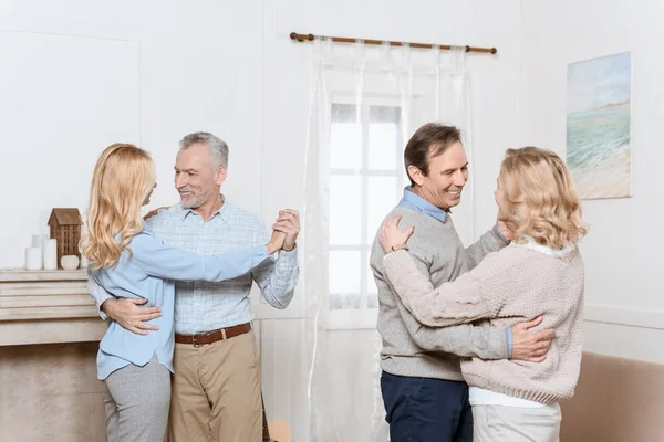 Hombres y mujeres de mediana edad bailando junto a la chimenea en una habitación acogedora - foto de stock