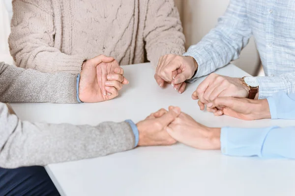Cropped image of friends mily sitting at table and holding hands of each other while praying — Stock Photo