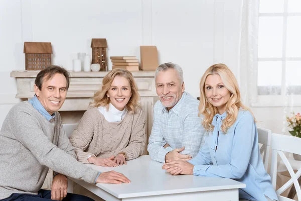 Glückliche Freunde, die am Tisch sitzen und in die Kamera schauen — Stockfoto