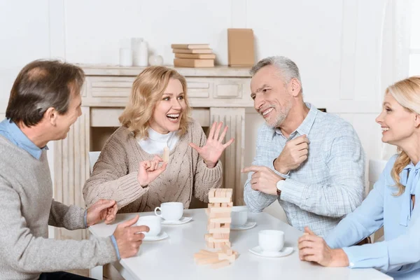 Amigos felices sentados en la mesa con té y jugando torre juego - foto de stock