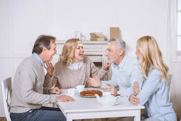 Freunde spielen Kartenspiel mit Worten auf der Stirn, während sie am Tisch sitzen — Stockfoto