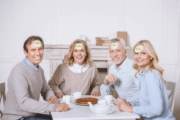 Freunde spielen Kartenspiel mit Worten auf der Stirn, während sie am Tisch sitzen — Stockfoto